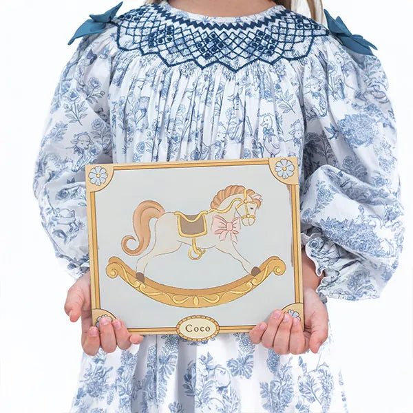 A child holding the Coco card in a blue smocked dress